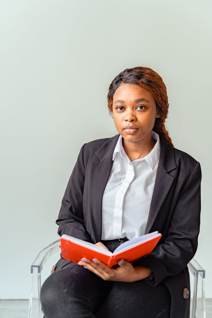 services-02 Portrait of a serious woman in professional attire holding a red book, posing indoors.